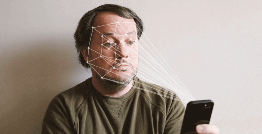 homem segurando celular em uma mão. Do celular saem linhas em direção a pontos de seu rosto simulando um aplicativo de reconhecimento facial.