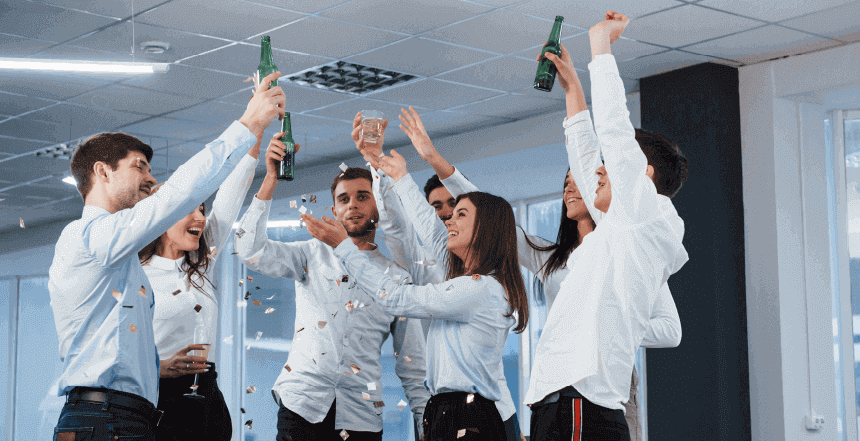 Imagem de pessoas de roupa social segurando garrafas e taças com líquido, enguendo-as para cima, representando uma confraternização de empresa.