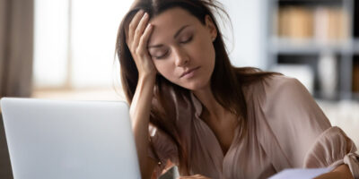Trabalhadora de frente para laptop de olhos fechados cansada por conta de férias vencidas