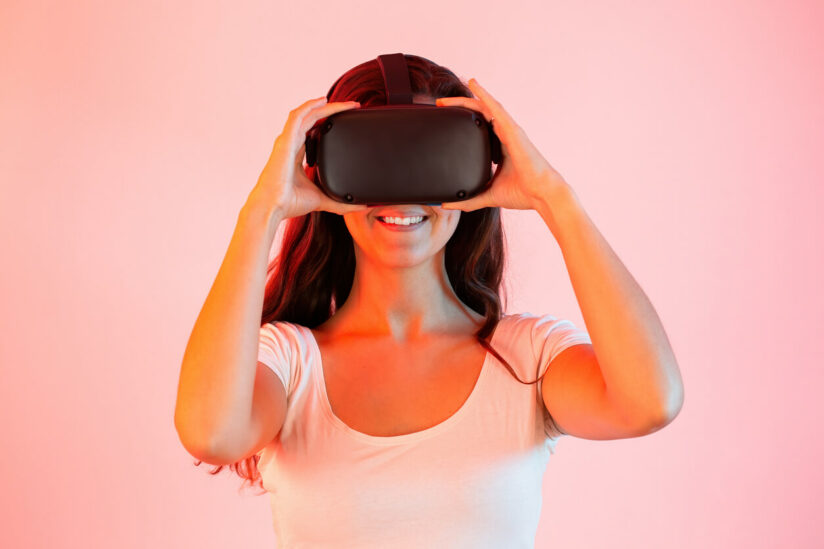 Mulher de frente segurando óculos de realidade virtual no rosto com as mãos enquanto acessa o metaverso