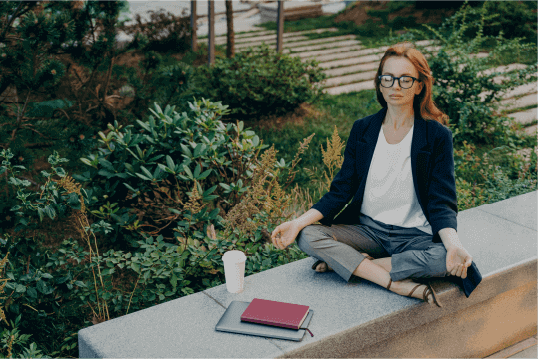 pessoa de roupa social com olhos fechados, pernas cruzadas e mãos sobre joelhos sentada em frente a notebook fechado simulando demissão silenciosa