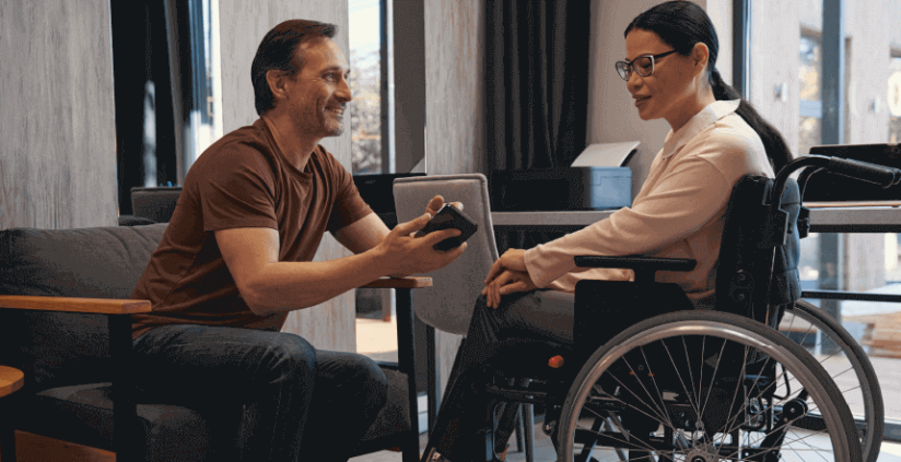 pessoa com deficiência, cadeirante, interagindo com outra pessoa em ambiente corporativo demonstrando como não praticar capacitismo